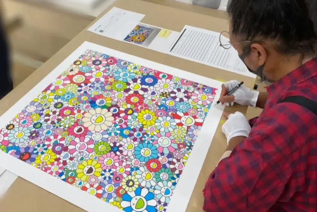 Takashi Murakami autographing a print, showcasing the artist's direct involvement in authenticating his artwork.